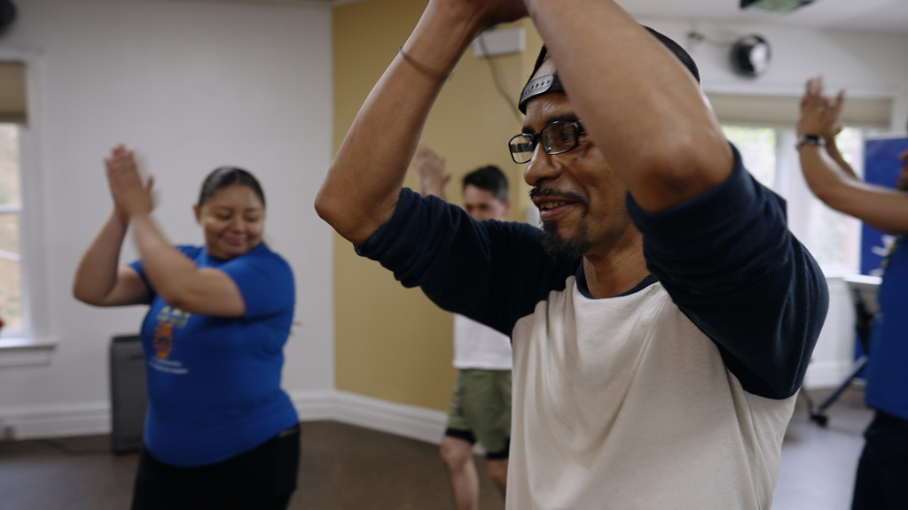 Man leading exercise class claps overhead.