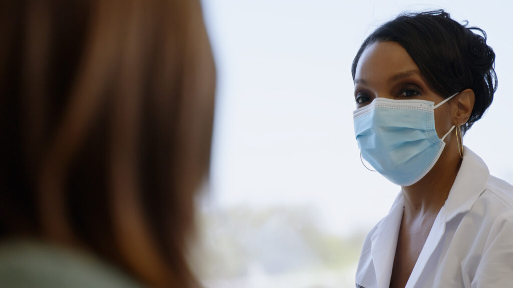 Female doctor wearing face mask looks at patient.