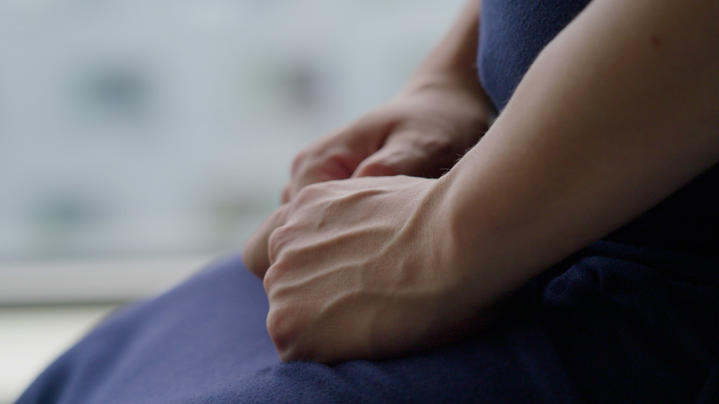 Close up view of hands as woman sits on exam table.