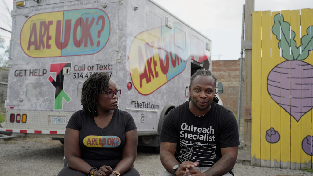 Two team members of the T sit outside at outreach location in St. Louis.