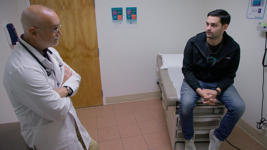 Doctor speaks with young male patient sitting on exam table.